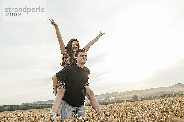 Young man piggybacking girlfriend in agricultural field