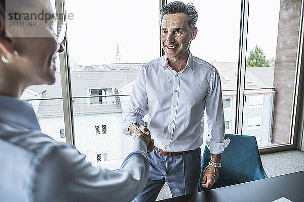 Happy businessman shaking hands with businesswoman in office