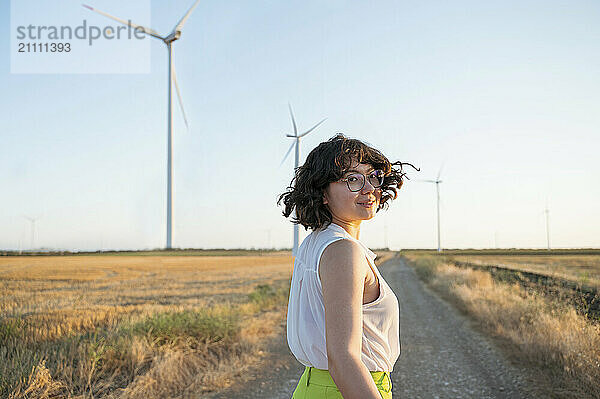 Young woman looking over shoulder at wind farm