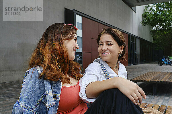 Happy lesbian couple sitting on bench in front of building