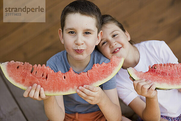 Smiling girl leaning on brother and eating watermelon at porch