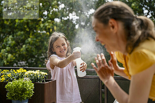 Cheerful daughter spraying water on mother in balcony