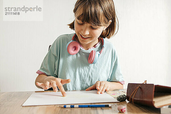 Smiling girl sitting near table and drawing on paper at home