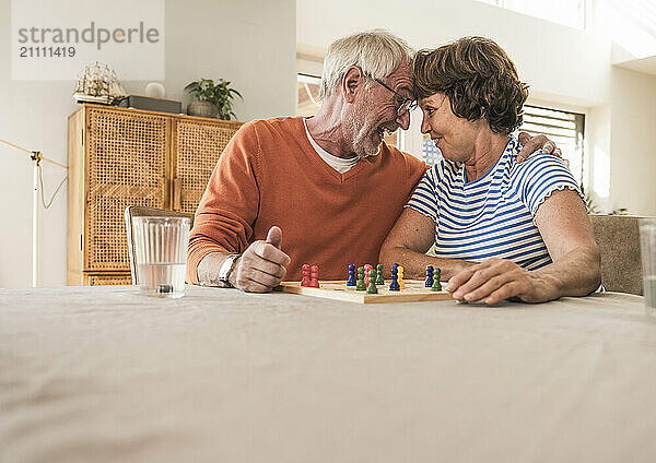 Senior couple sitting face to face and playing board game at home