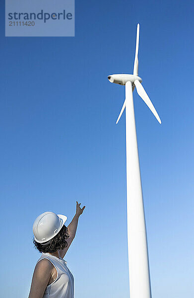 Engineer reaching hand at wind turbine under sky