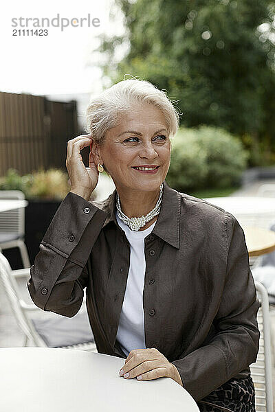 Smiling woman with hand in hair sitting near table in cafe