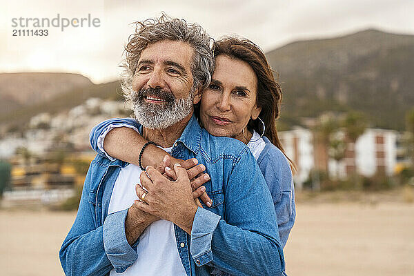 Senior woman embracing man from behind at beach