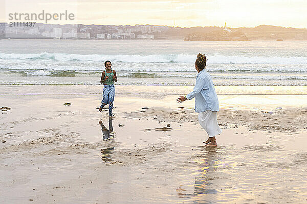 Girl running towards grandmother during sunset at beach