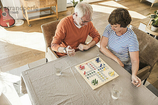 Senior couple sitting near table and playing ludo at home