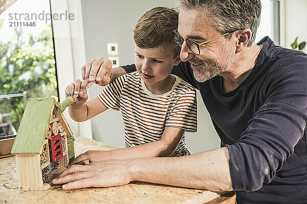 Boy painting model house by grandfather on table