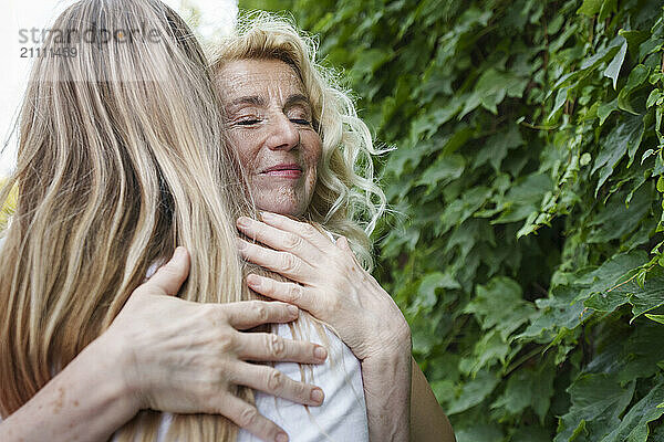 Smiling senior woman hugging daughter near plants