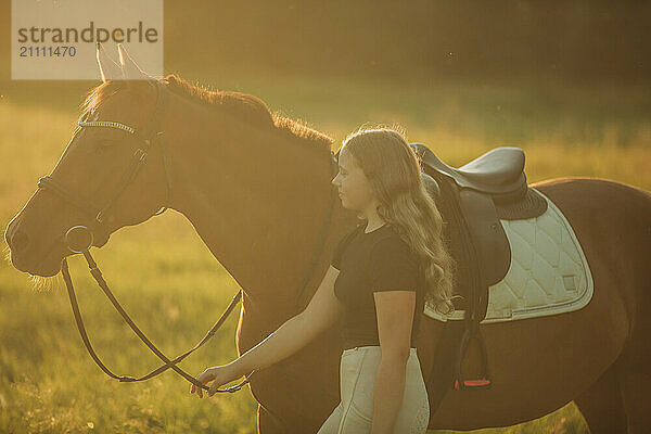 Girl with horse walking in meadow on sunny day