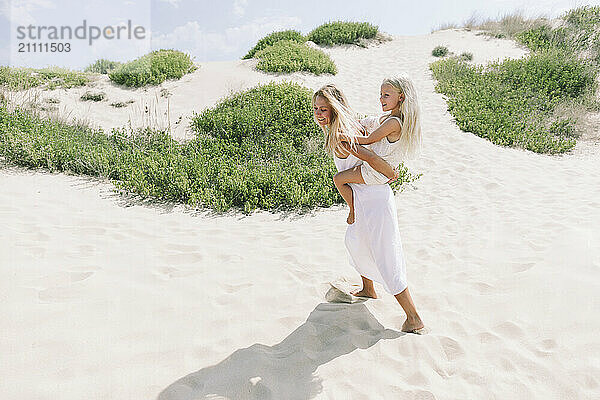 Mother giving piggyback ride to daughter at beach on sunny day