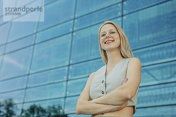 Confident blond woman standing with arms crossed outside building