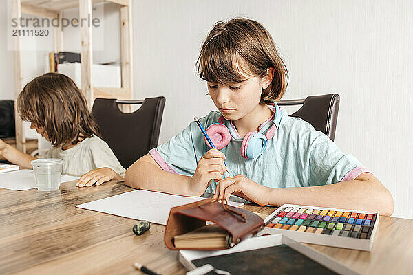 Girl holding pencil and sitting near table with brother at home