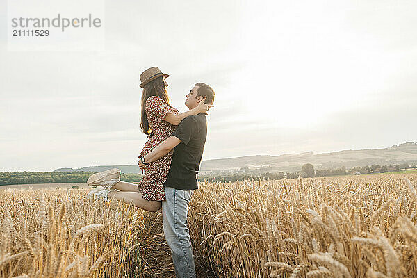 Man picking up girlfriend under sky in spikelet field