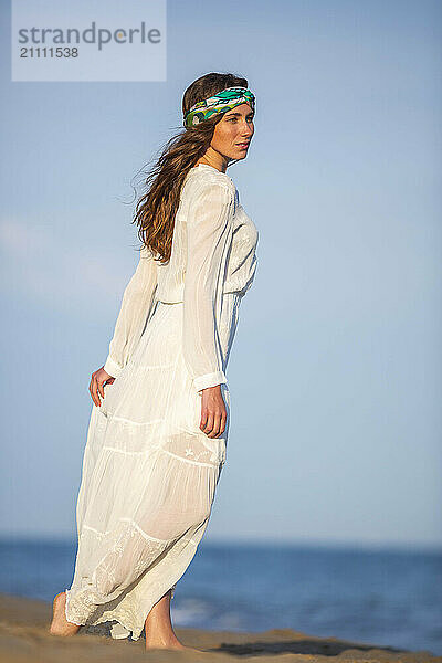 Contemplative woman in white dress looking over shoulder at beach