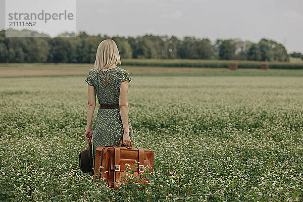 Blond hair woman standing with suitcase in field