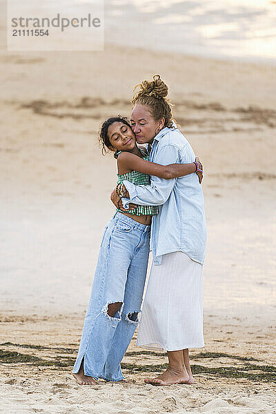 Mature woman and granddaughter embracing at beach