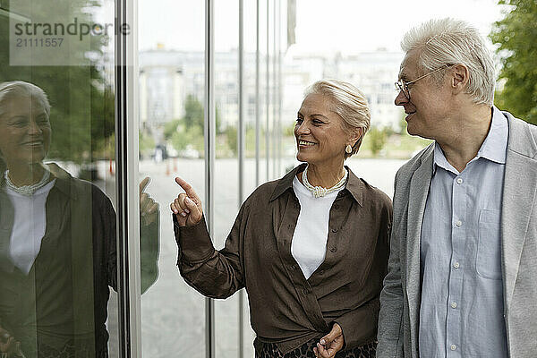 Senior man with woman pointing at glass wall in street