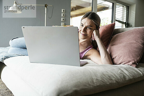 Smiling young woman using laptop on sofa at home