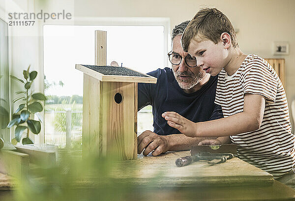 Boy making birdhouse with grandfather at home