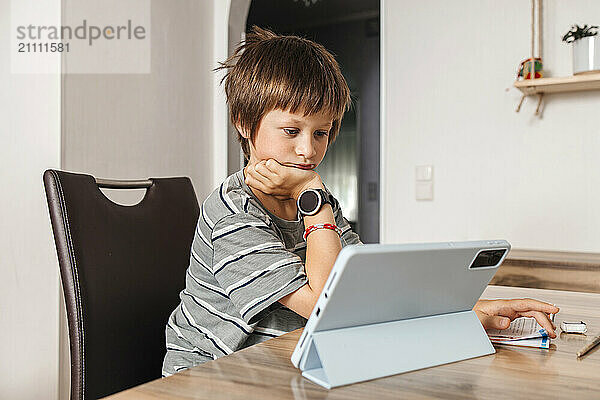 Boy sitting near table and watching on digital PC at home