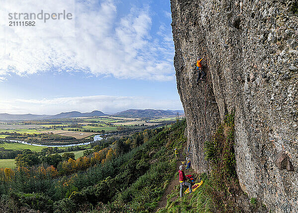 Mature rock climbers climbing rock under cloudy sky