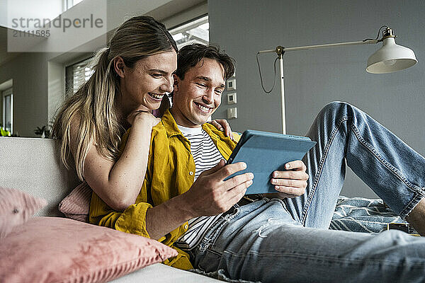 Happy young woman leaning on boyfriend using tablet PC on sofa at home