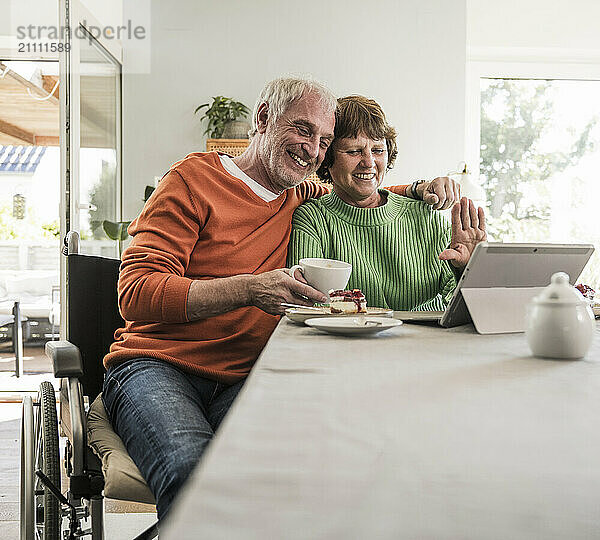 Smiling senior couple sitting near table and using digital PC on table at home