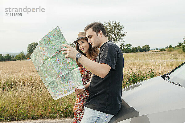 Couple standing and looking at map near car