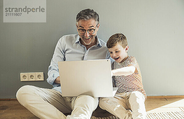 Happy grandfather using laptop by grandson at home