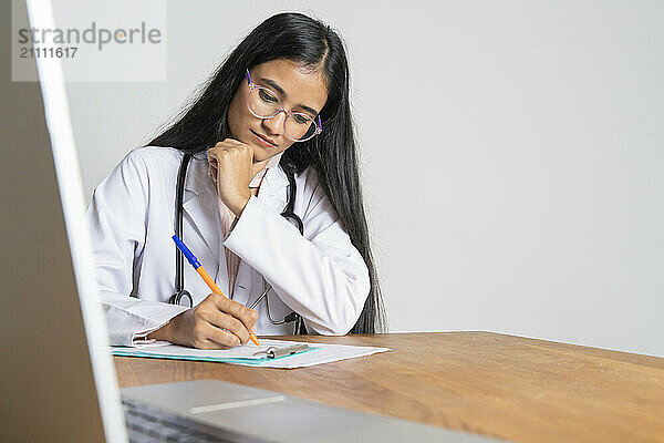 Young doctor sitting near table and writing prescription at clinic