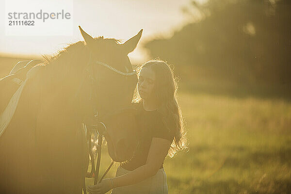 Girl with horse standing in meadow on sunny day