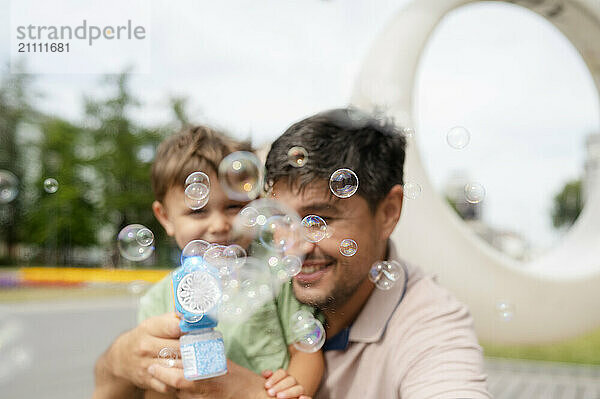 Father and son playing with bubble gun at park