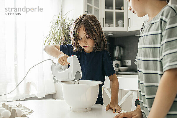 Boy using electric mixer with brother in kitchen