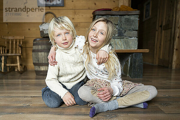 Happy boy and girl sitting on hardwood floor in chalet