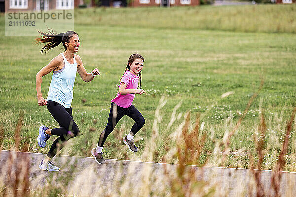 Happy mother and daughter spending leisure time running on footpath