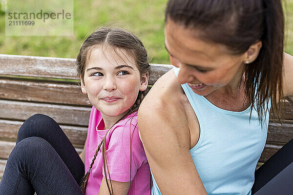 Smiling daughter sitting back to back with mother on bench