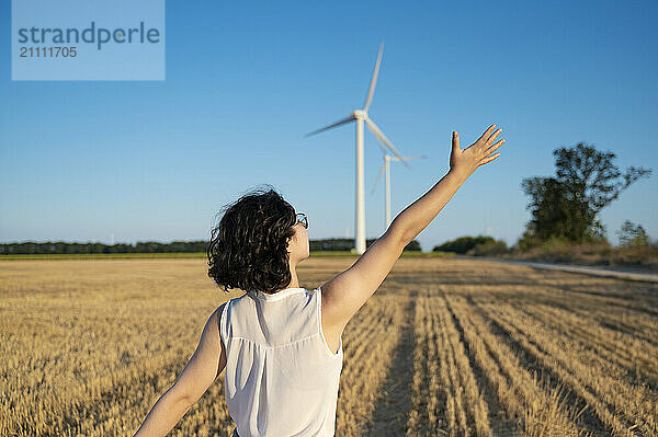 Engineer with hand raised standing in wind turbine field