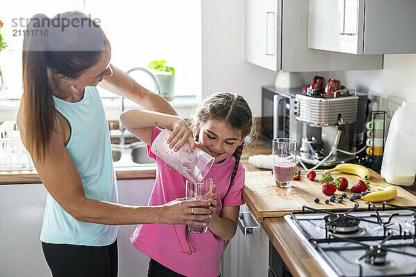 Mother with daughter pouring milkshake in glass at home