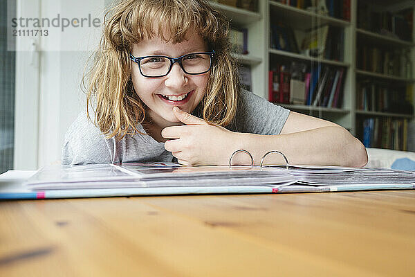 Happy girl sitting with photo album at table