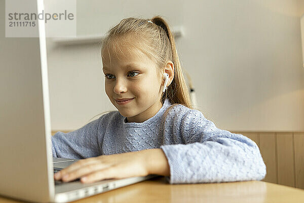 Happy girl sitting near table and using laptop at home