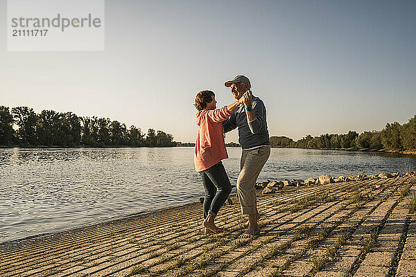 Senior couple holding hands and dancing near river on sunny day