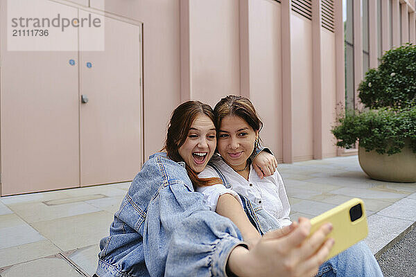 Gay couple taking selfie and sitting on sidewalk