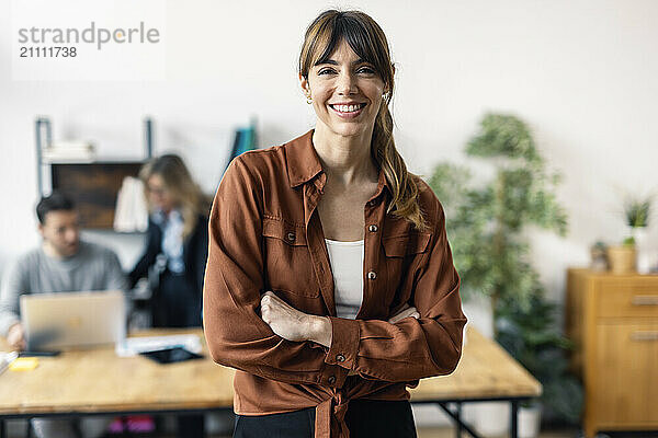 Happy businesswoman with arms crossed standing in office