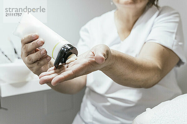 Massage therapist squeezing moisturizer on hand at spa