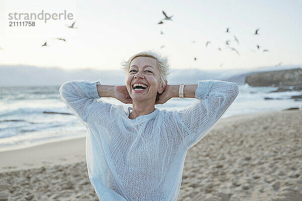 Cheerful mature woman with hands behind head at beach