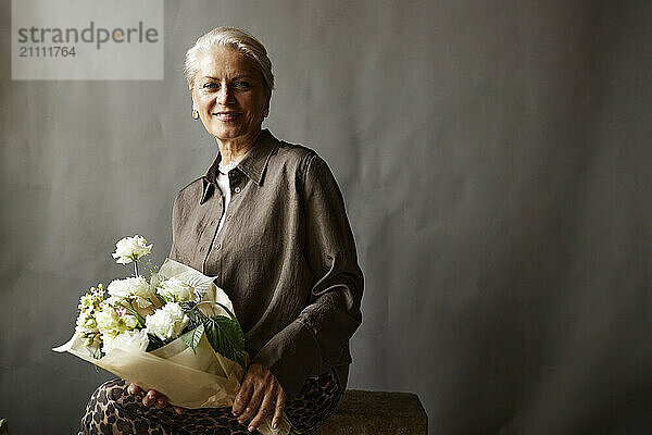 Smiling woman with bouquet of flowers against gray background