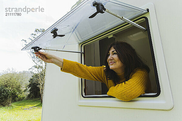 Smiling senior woman opening window of motor home